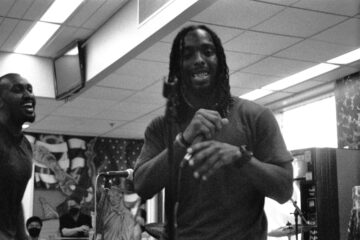 black and white photo of musician smiling down at camera with industrial lights of correctional housing shining above