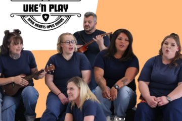 5 women and 1 man dressed in inmate blue singing and playing ukuleles