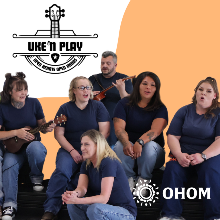 5 women and 1 man dressed in inmate blue singing and playing ukuleles