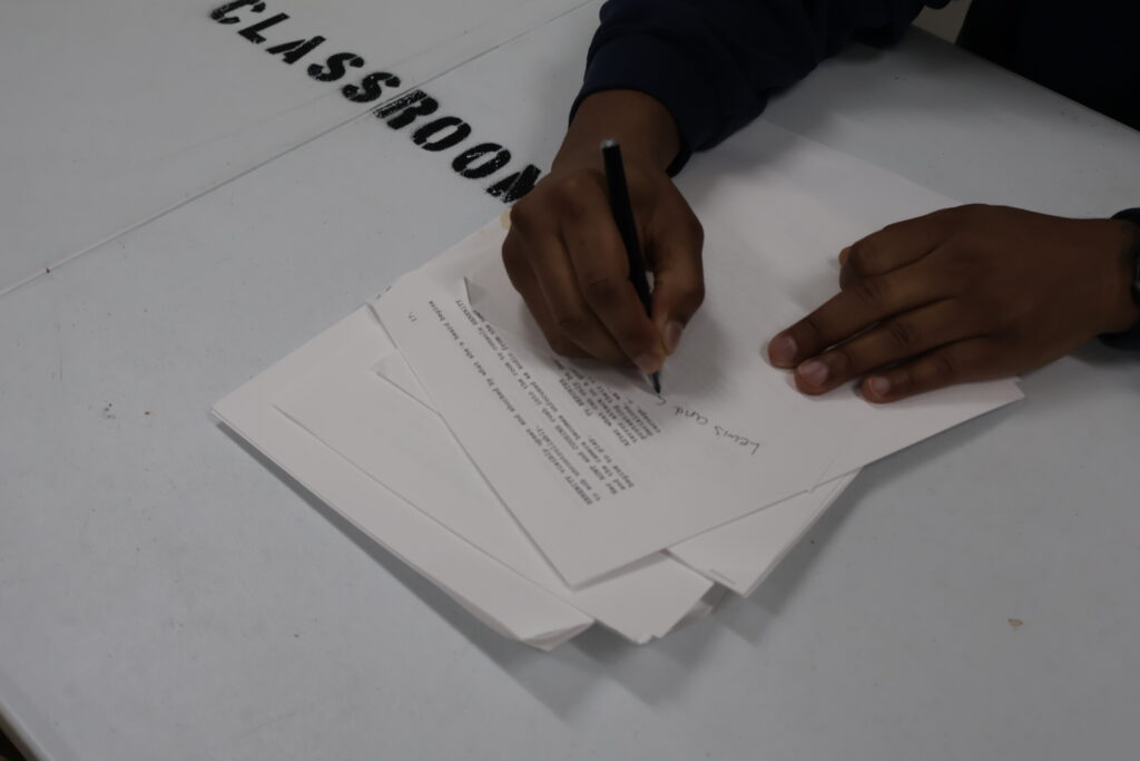 hands on paper. editing a script. on white table marked CLASSROOM in big black letters