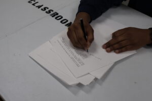 hands on paper. editing a script. on white table marked CLASSROOM in big black letters