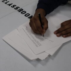 hands on paper. editing a script. on white table marked CLASSROOM in big black letters