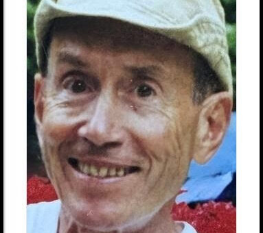 looking directly into the camera and smiling while sporting a traveler's cap