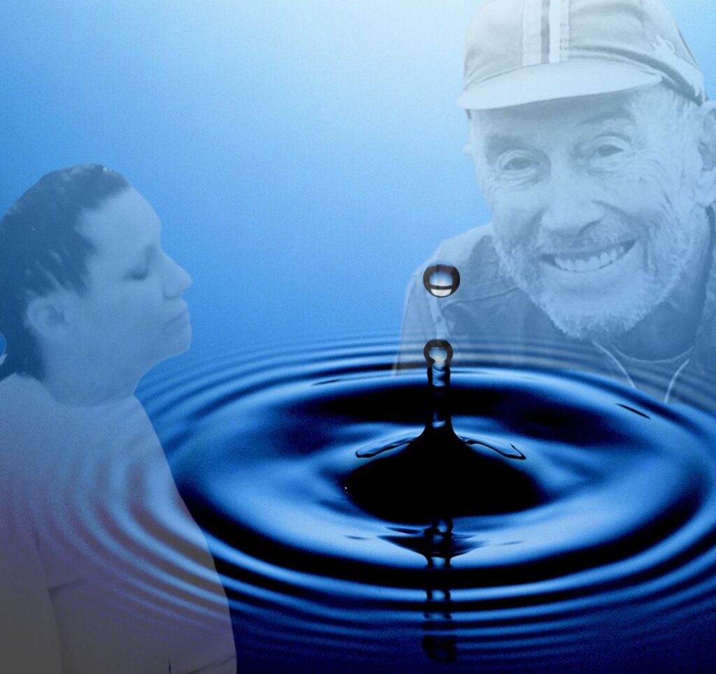 Jerry smiles directly into the camera. Denise has her eyes closed with a contented look. A water droplet ripples between them