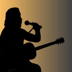 golden glow behind fella singing into a mic and holding a guitar