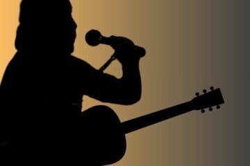 golden glow behind fella singing into a mic and holding a guitar