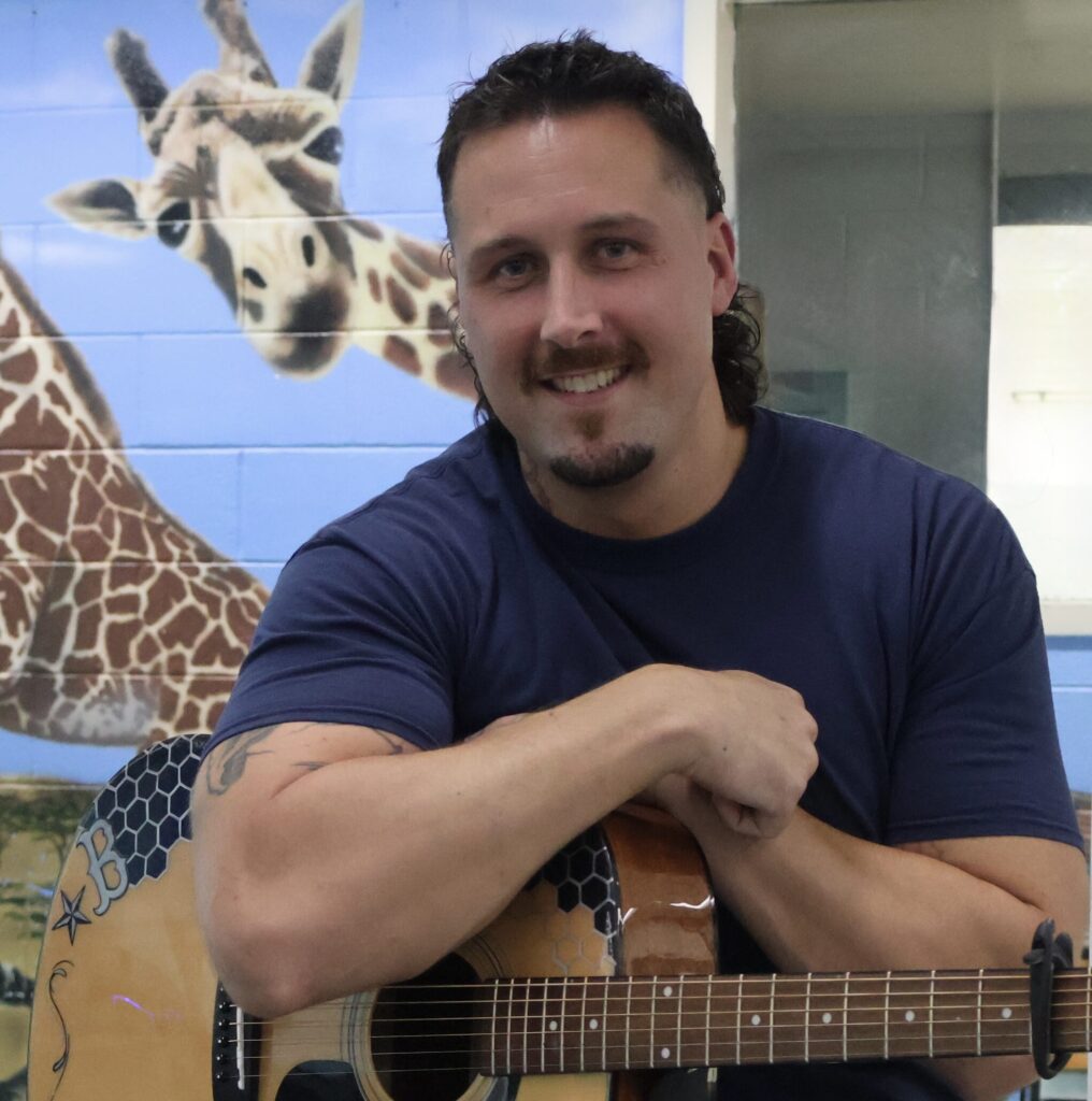 fella holding his guitar and smiling at the camera. a painting of a giraffe looking at us over his shoulder
