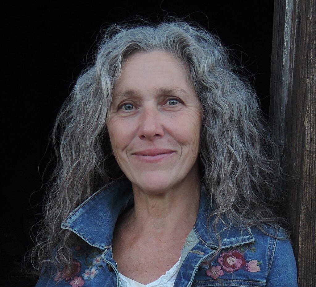 Woman smiling with wavy light hair, wearing a white shirt and blue jean jacket