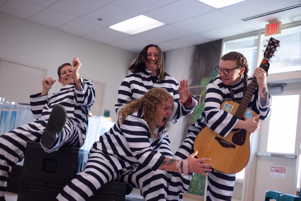 4 women in a reactionary pose dressed in ‘Clooney’ style black n white prison clothes