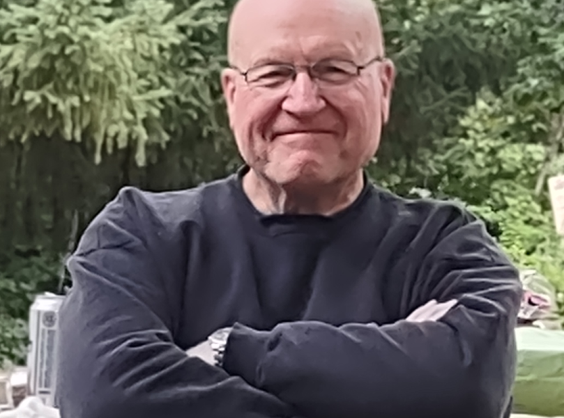 Dick lounging on a park bench with a big grin on his face, arms and legs crossed.